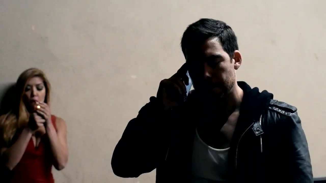 David Wachs on a phone in a leather jacket while a woman in a red dress lights a cigarette in the background, from Down Tempo