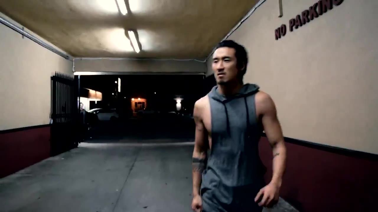 Jasper Jeon walking toward camera in a sleeveless hoodie under fluorescent alley lights, from Down Tempo