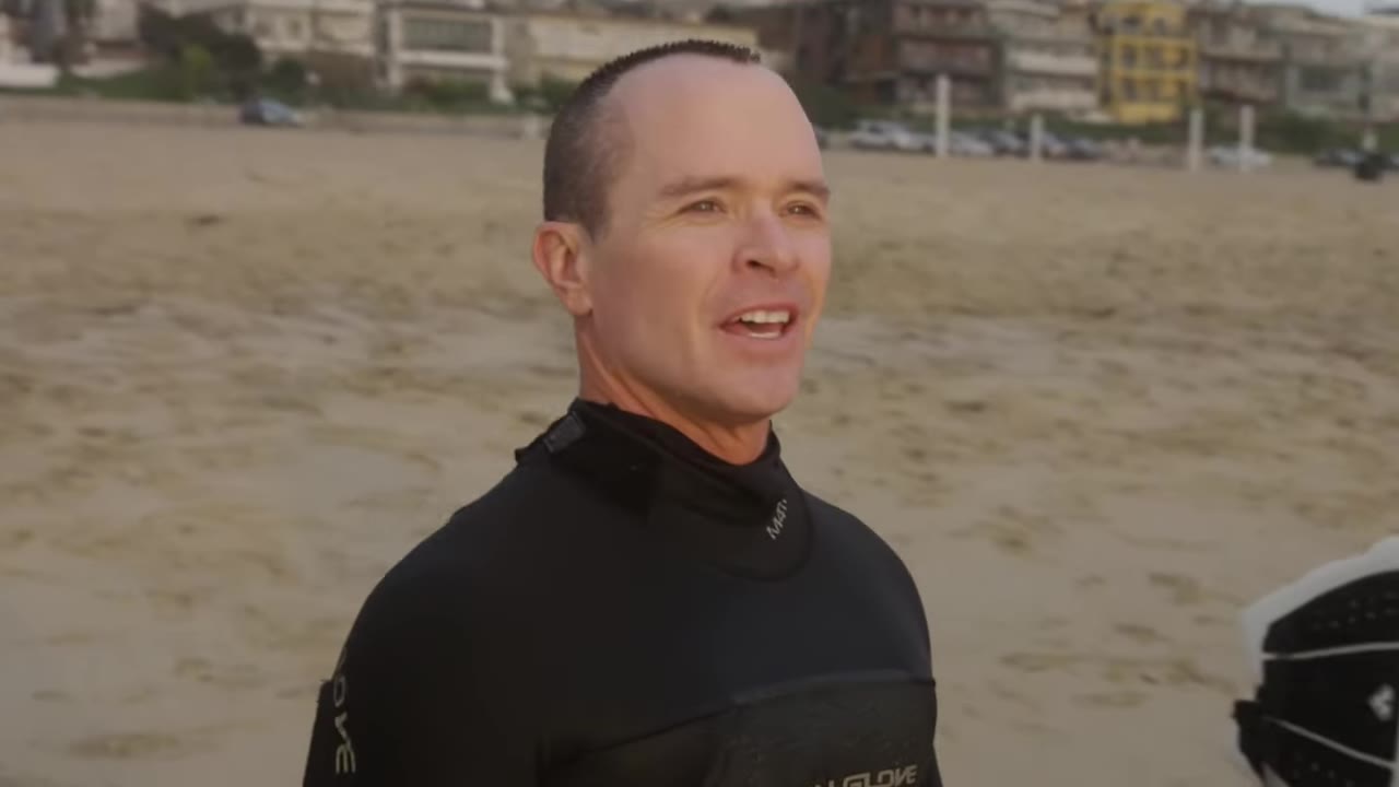 McKay Stewart in a black wetsuit on the beach, mid-conversation
