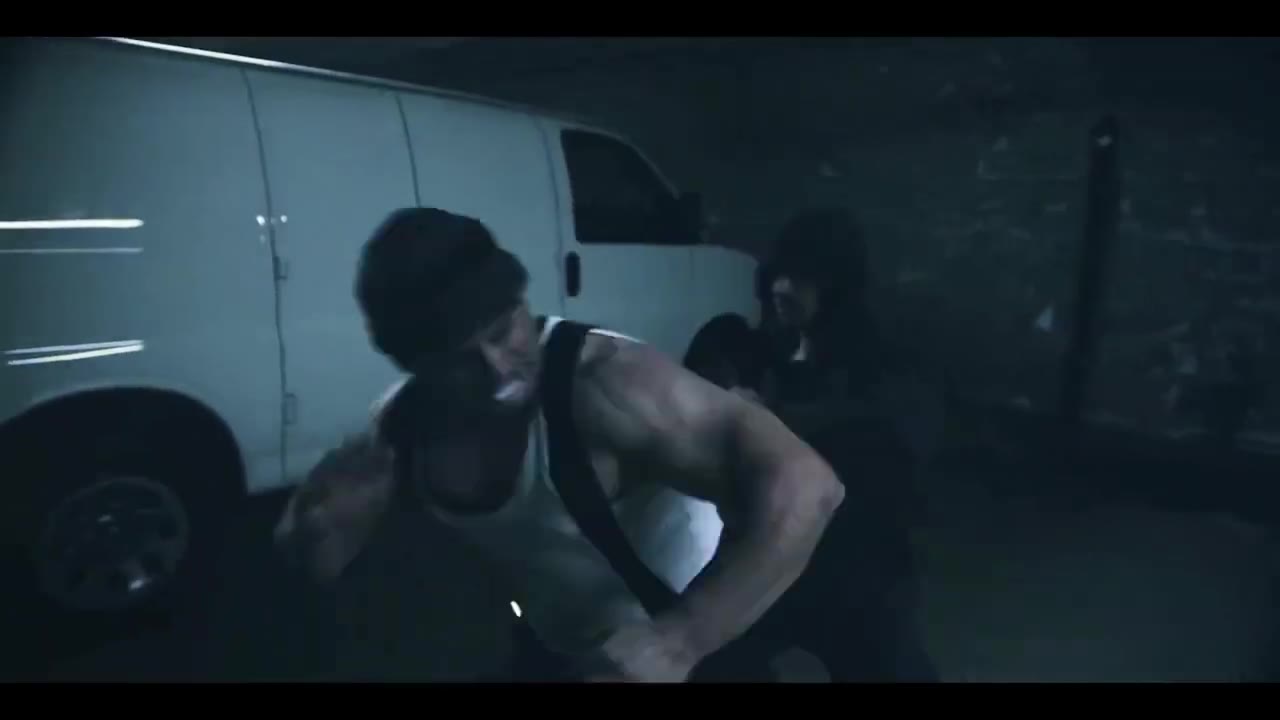 Close shot of a muscular fighter in a tank top grappling with the hooded fighter beside the van
