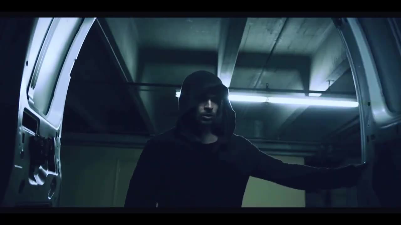 McKay Stewart in a dark hoodie stands in the open back doors of a white van inside a parking garage, in a frame from the GLITCH teaser