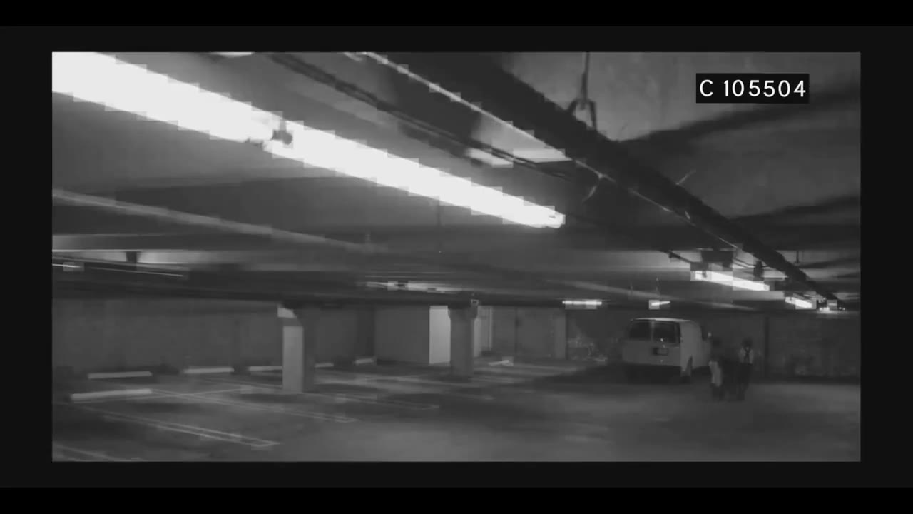 Grainy black-and-white security camera view of an empty parking garage with a timecode in the corner